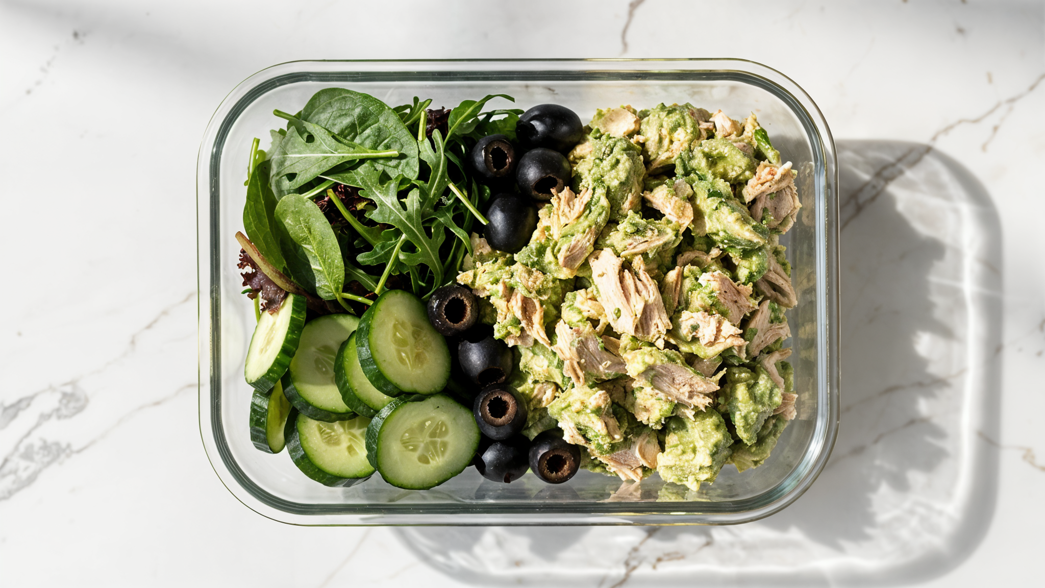 Avocado chicken salad with cucumbers, olives, and greens in a meal prep container